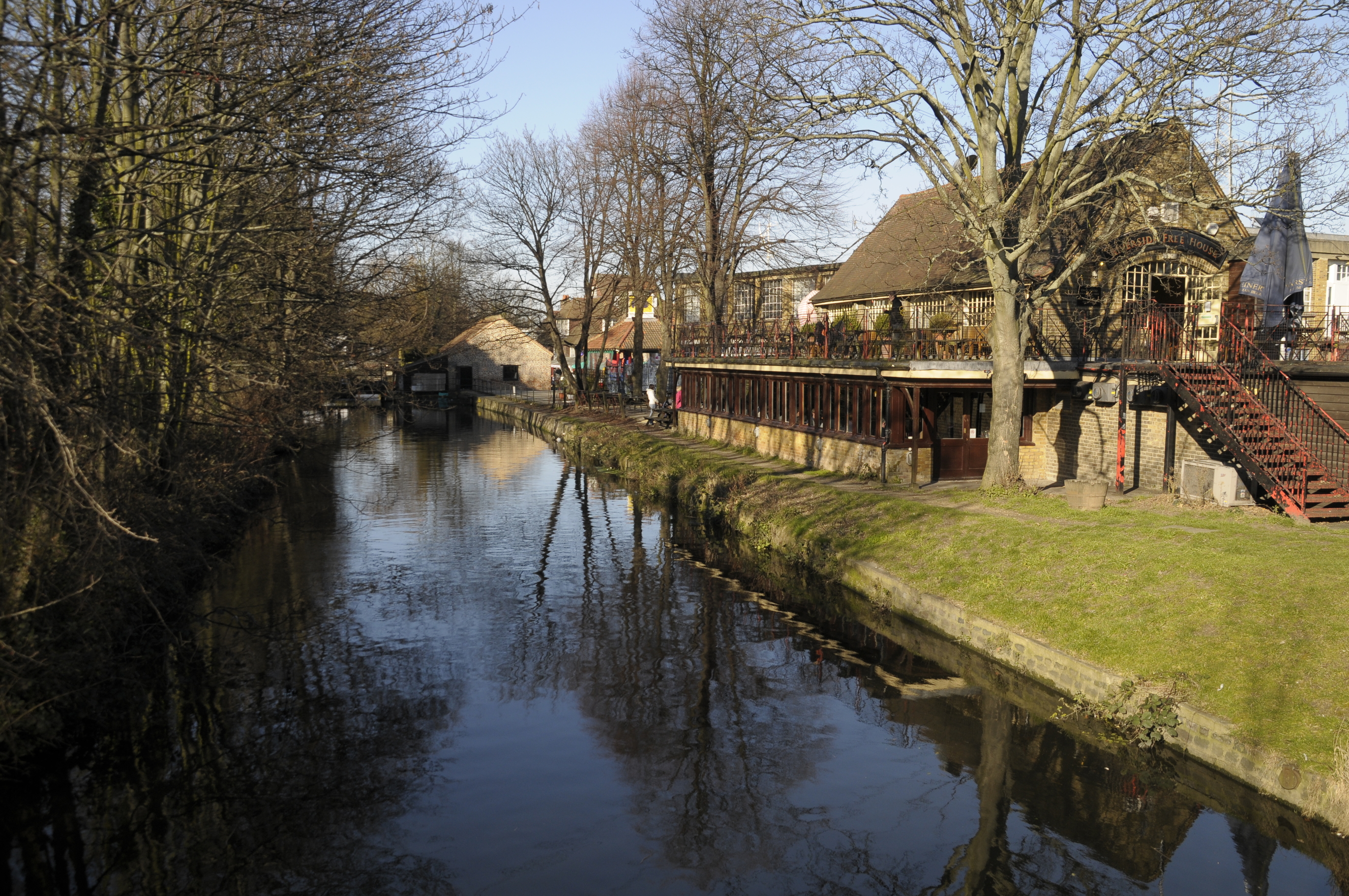 River Wandle beside Merton Abbey Mills, with waterside paths and historic mill buildings reflected in the water.
